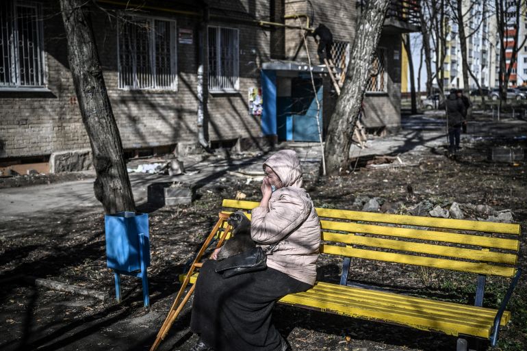 A crying woman sits on a bench outside a building damaged by bombing in the Ukrainian city of Kharkiv