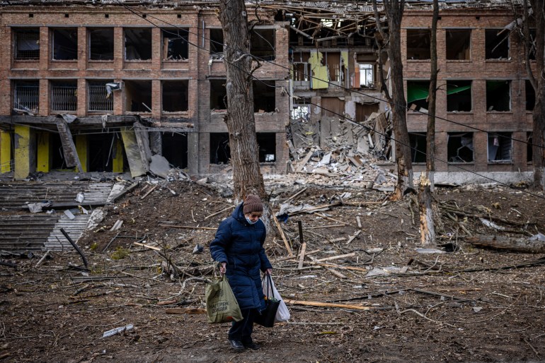 A woman walks in front of a destroyed building.