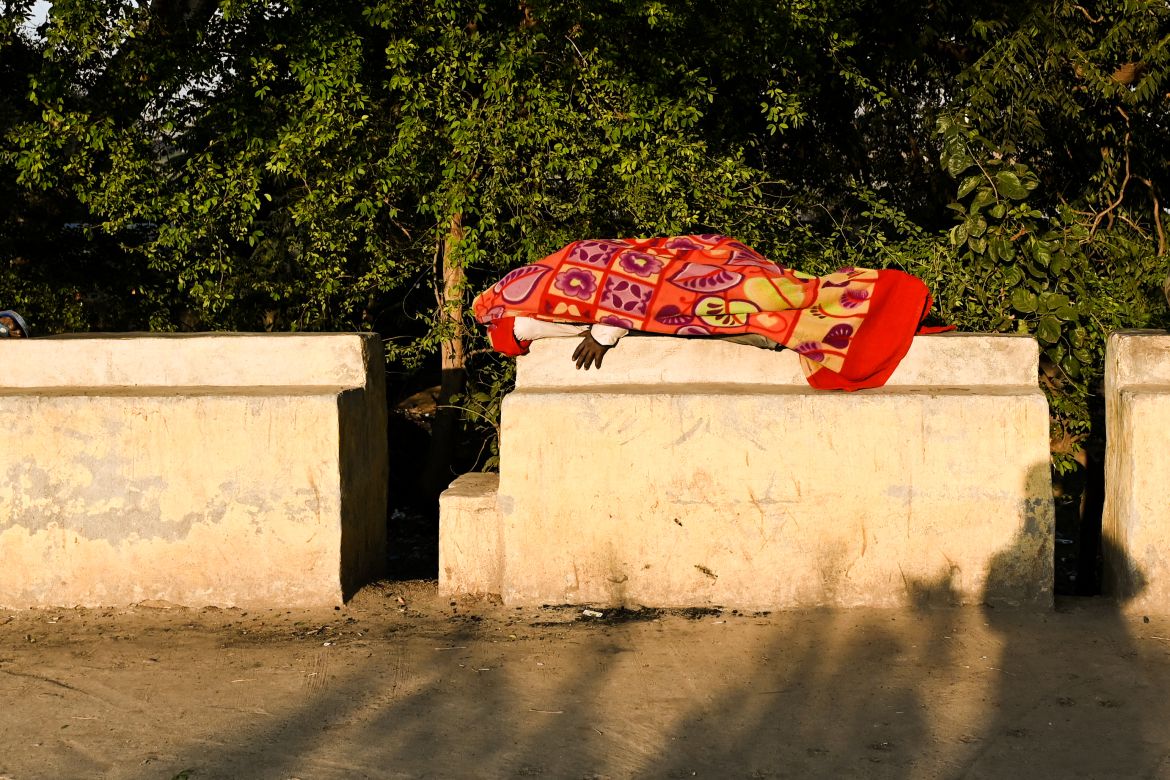 In this picture taken on January 29, 2022, shows a homeless man sleeping on the boundary railing of a sidewalk near a government-run shelter in New Delhi.