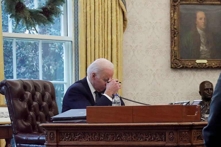 U.S. President Joe Biden is seen through a glass doorway as he speaks by phone with Ukraine's President Volodymyr Zelenskiy in the Oval Office at the White House in Washington, U.S`