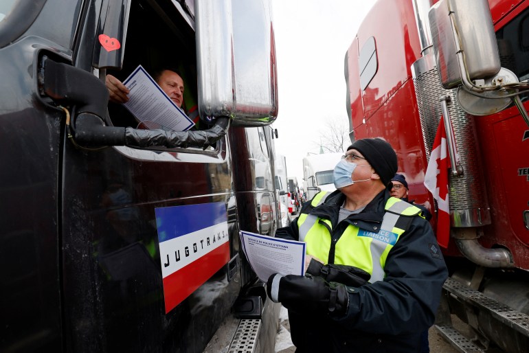 A police officer hands an information sheet to a truck driver in his vehicle