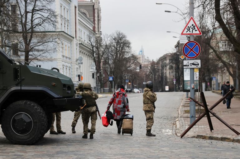 A woman walks past Ukrainian military service members guarding a road that leads to a government block