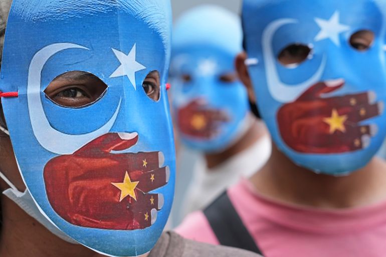 A close up of the faces of three students wearing masks in the colour of pro-independence East Turkistan flag with a hand in the colour of a Chinese flag over their mouths