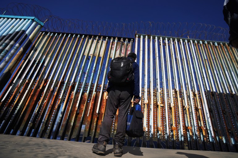 Migrants standing beside border wall