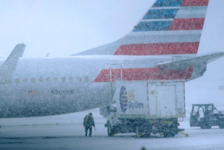 Snow falls on a ground crew working outside a parked plane at Dallas Fort Worth International Airport .