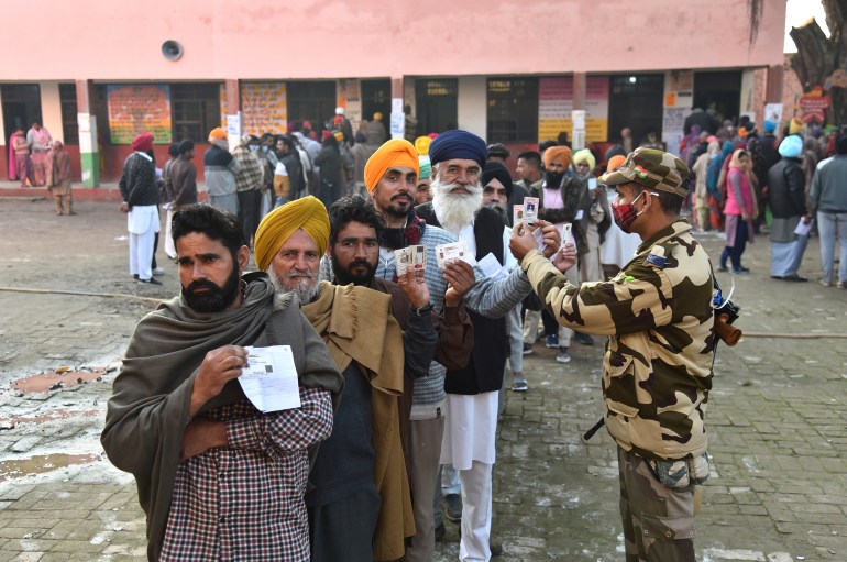 A paramilitary soldier checks identity cards of voters standing in a queue outside a polling station