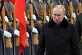 Vladimir Putin, in heavy black winter coat, walks in front of a soldiers standing to attention