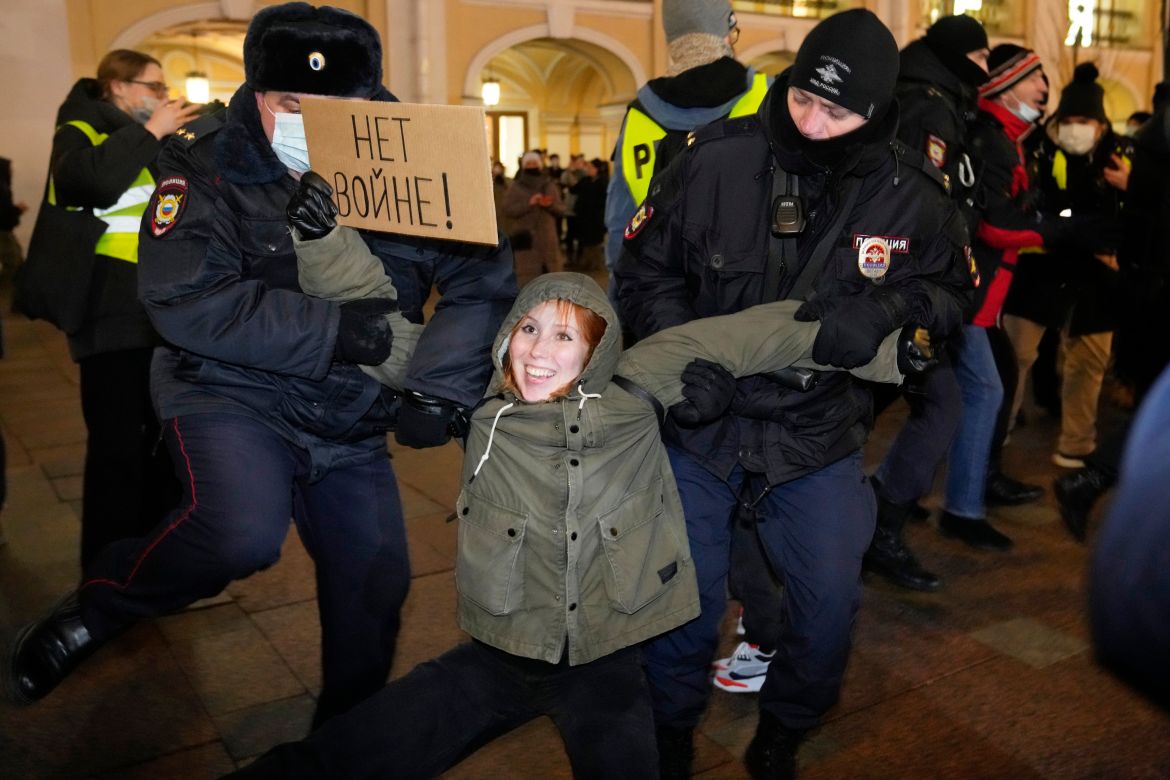 Police officers detain a demonstrator holding a sign reading 'No war!'