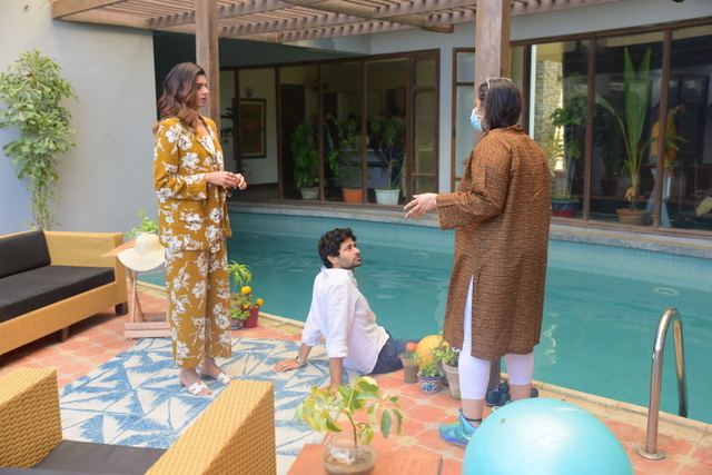 A photo of Meenu Gaur talking to two actors near a pool, a man and a woman. The man sits with his feet in the pool and the woman stands behind him with Meena in front of the both of them.