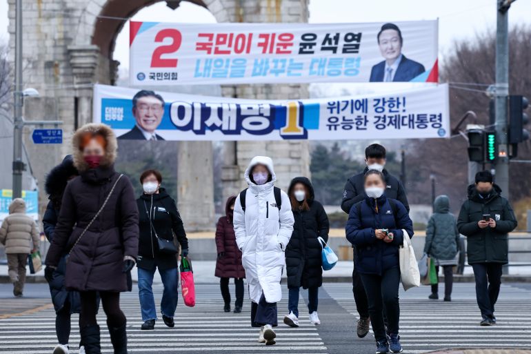 People in winter coats cross the street beneath election banners for South Korea's two main election candidates