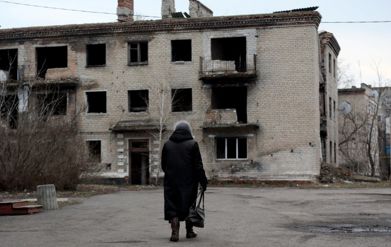 A woman walks past an old destroyed building in small town of Krasnogorivka, Donetsk region
