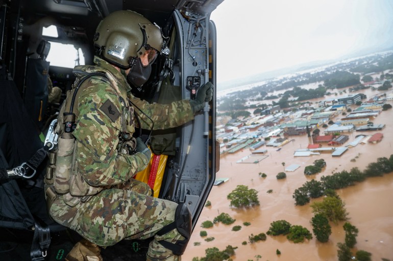 A soldier looks down from a helicopter on an inundated Lismore