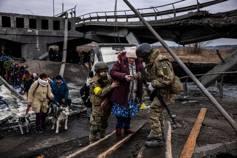 Ukrainian soldiers help an elderly woman to cross a destroyed bridge as she evacuates the city of Irpin