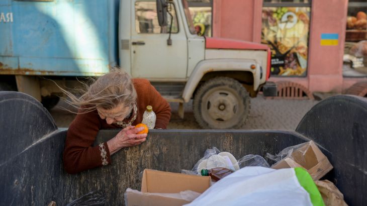 A Ukrainian woman looks for food in a rubbish-bin