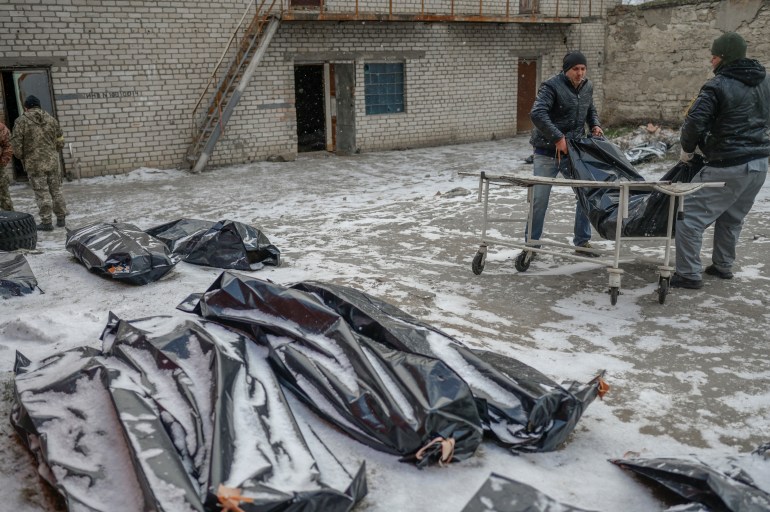 Two men carry a corpse in a body bag to lay it next to others in a snow covered yard in Mykolaiv,