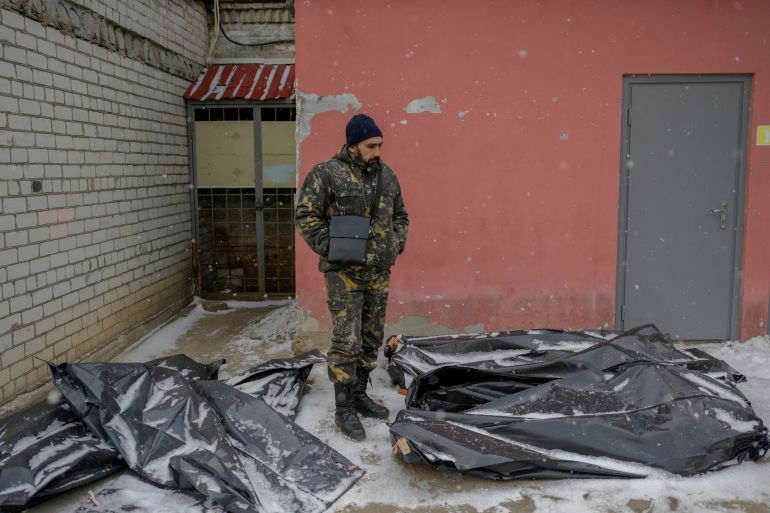 A Ukrainian man in camouflage stands next to snow covered body bags in the yard of a morgue in Mykolaiv,