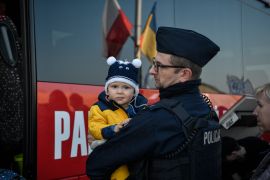 A Polish police officer holds a child to help his mother while board a bus for their further transportation after crossing from Ukraine into Poland at the Medyka border crossing on March 15, 2022. - More than three million people have now fled Ukraine since Russia invaded on February 24, the United Nations said on March 15, 2022. (Photo by Louisa GOULIAMAKI / AFP)