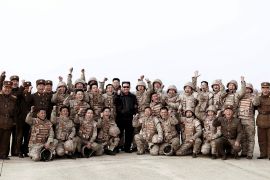 Kim Jong Un, dressed in black leather bomber jacket and dark glasses, poses with member of the armed forces