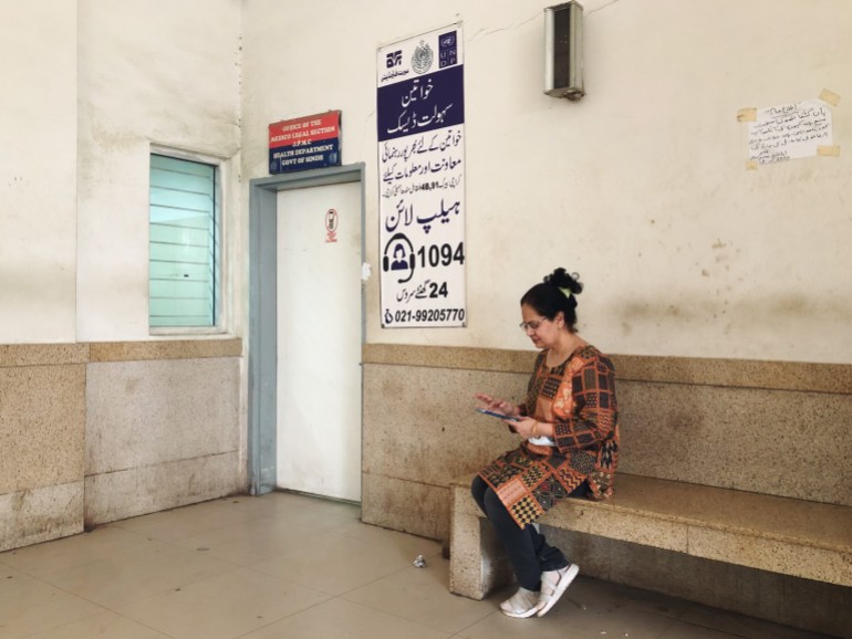 A photo of Dr Summaiya sitting outside the room where female patients/victims are taken to be examined, sitting on a bench and looking at her phone.