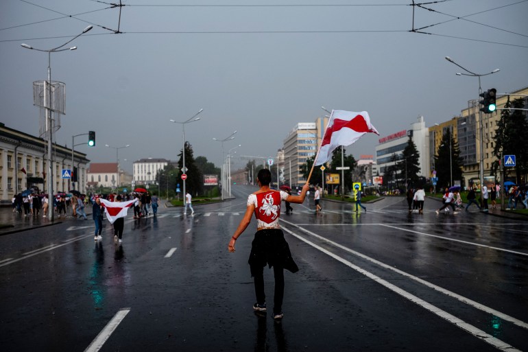 A photo of a woman walking down a street holding the Belarus flag in one hand.