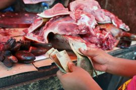 Customer holding bank notes in front of meat on chopping board
