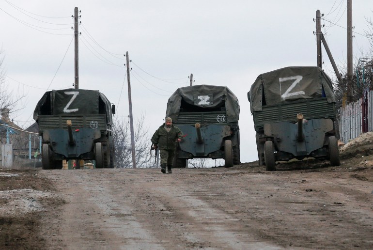 A service member of pro-Russian troops in a uniform without insignia walks past trucks with the letter "Z" painted on tent tops in the separatist-controlled settlement of Buhas