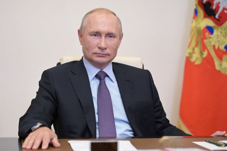 Russian President Vladimir Putin is seen sitting at a table