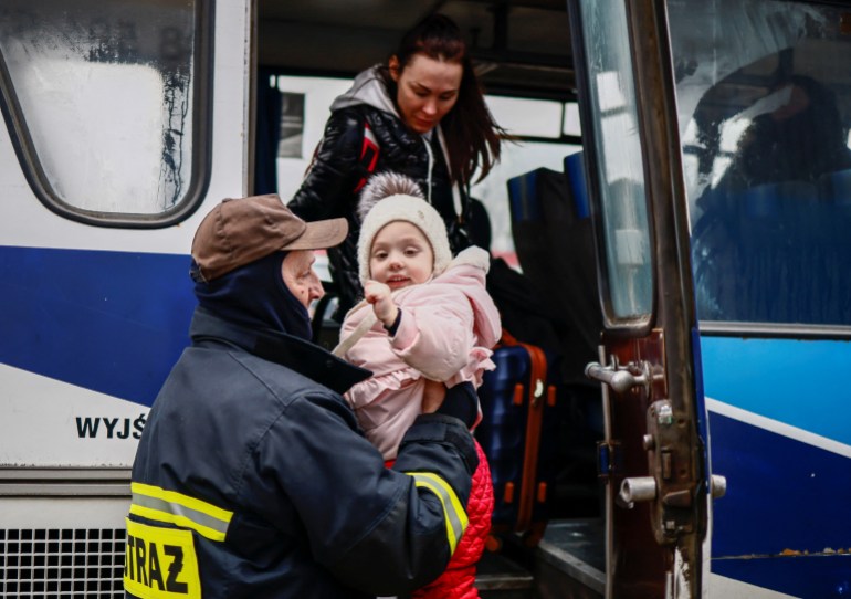 A Polish firefighter helps a Ukrainian child get off a bus.