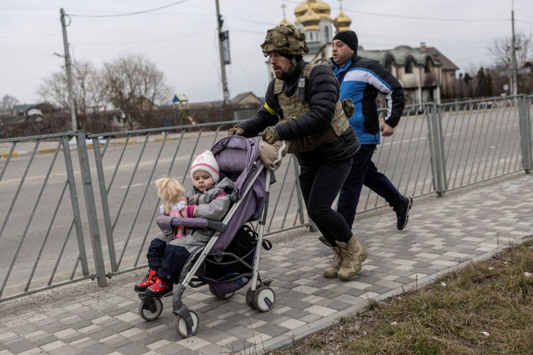 A service member of the Ukrainian armed forces helps to evacuate a child from the town of Irpin, on the only escape route used by locals after days of heavy shelling, while Russian troops advance towards the capital, in Irpin, near Kyiv