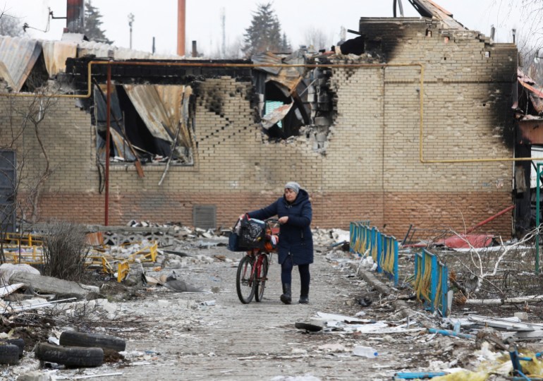 A woman walks with a bicycle next to a damaged building in Donetsk region, Ukraine