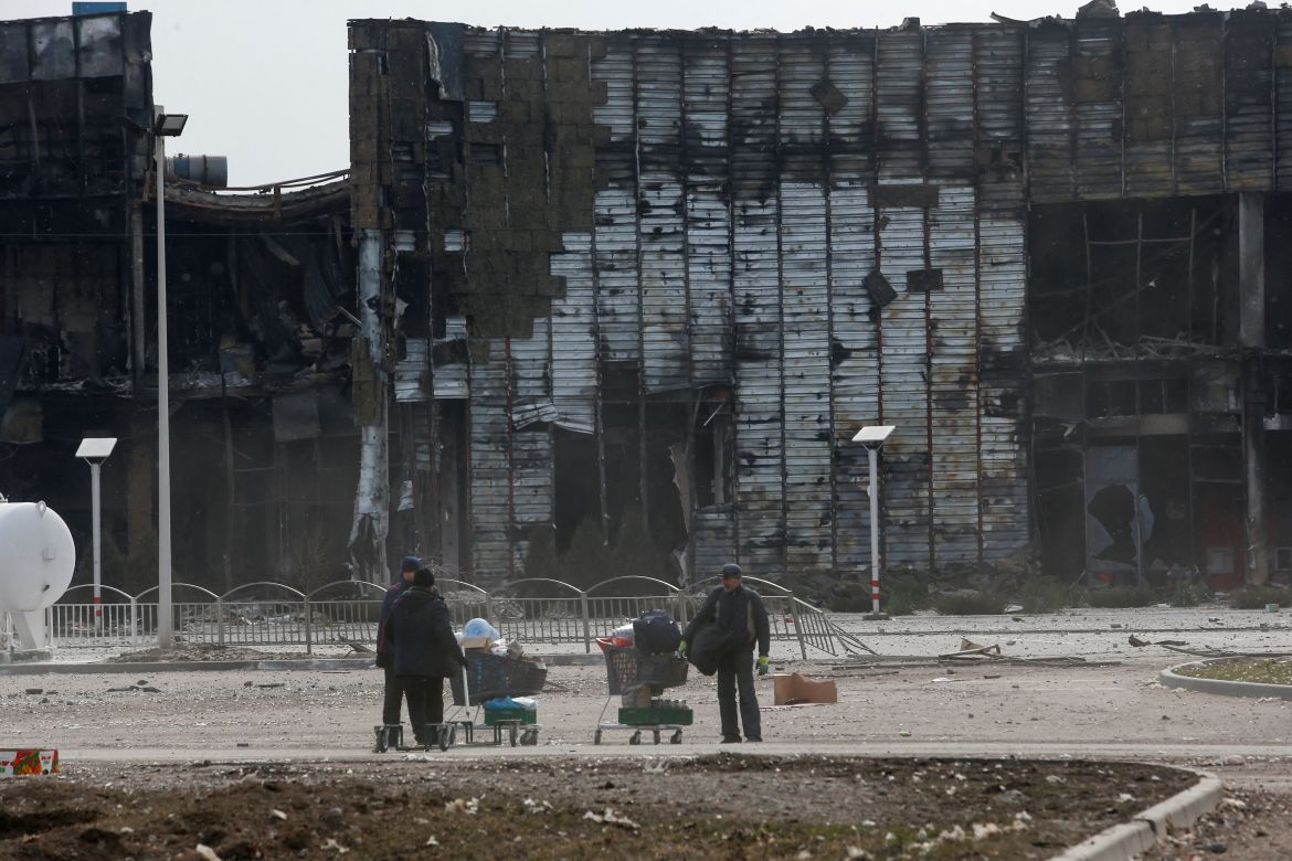 People use carts to transport belongings near a building, which was destroyed during Ukraine-Russia conflict in the besieged southern port city of Mariupol