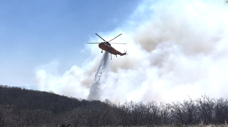 A firefighting helicopter makes a water drop on flames as the Eastland Complex wildfire 