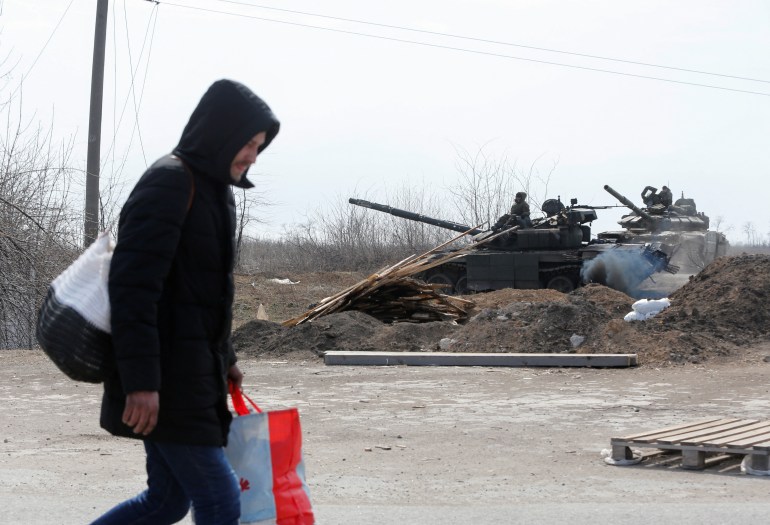 A man carries his belongings past a Russian tank
