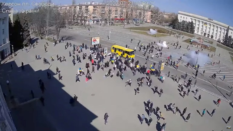 CCTV footage appears to show Russian troops (top, near building) firing stun grenades into a crowd of protesters, some with Ukrainian flags, amid the Russian invasion, along Ushakova Avenue in Kherson