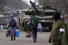 Civilians trapped in Mariupol city walk in front of a tank as they are evacuated.