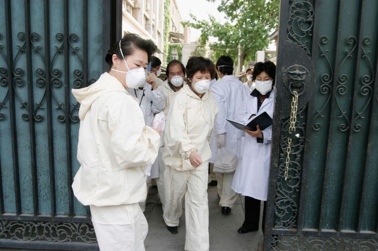 BEIJING, CHINA - APRIL 30: Quarantined medical workers, wearing face masks to protect against the Severe Acute Respiratory Syndrome (SARS) virus rush out of the entrance gate of the national institute of virology to pick up clothes and lunch boxes, on April 30, 2004 in Beijing, China.