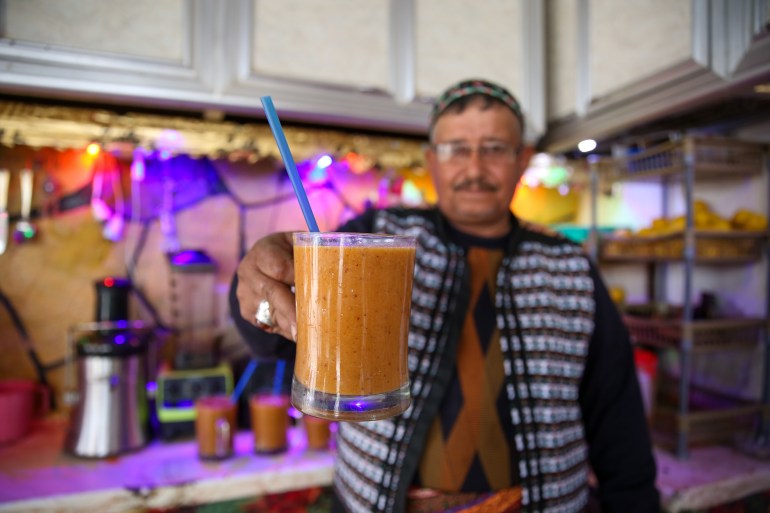 Daaboul holds out a glass mug of fruit cocktail with a blue straw in it.