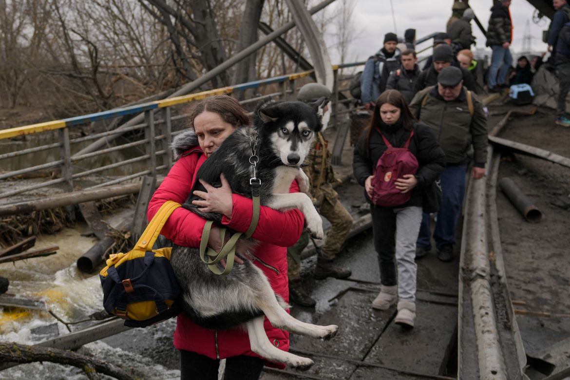 A woman holds a dog while crossing the Irpin River on an improvised path under a bridge that was destroyed by a Russian airstrike