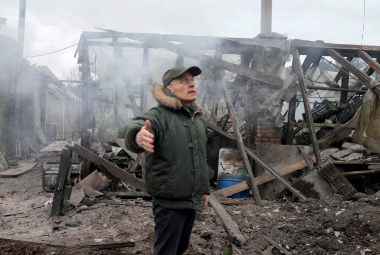 A man opens his arms as he stands near a house destroyed by Russian artillery shelling in Ukraine.