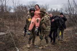 A woman carried by Ukrainian soldiers crosses an improvised path while fleeing the town of Irpin