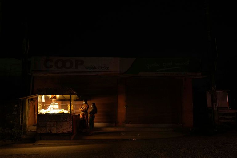 A Sri Lankan street food vendor serves customers outside a closed shop due to power cuts in Hendala