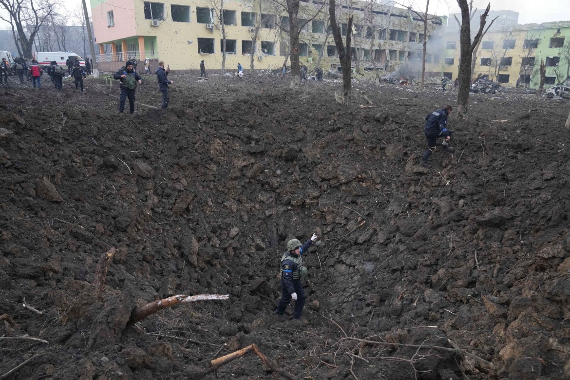 Ukrainian soldiers and emergency employees work at the side of the damaged by shelling maternity hospital