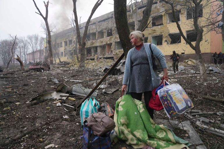 A woman walks outside a maternity hospital that was damaged by shelling in Mariupol [Evgeniy Maloletka/AP]