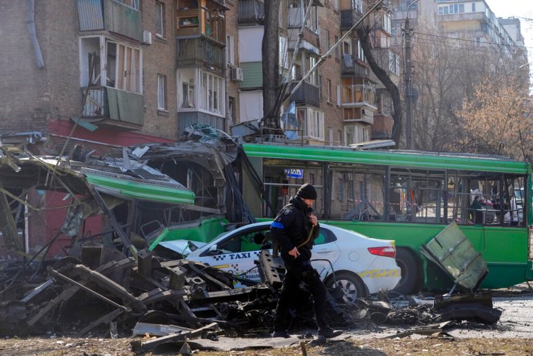A Ukrainian soldier passes by a destroyed a trolleybus and taxi after a Russian bombing attack in Kyiv.