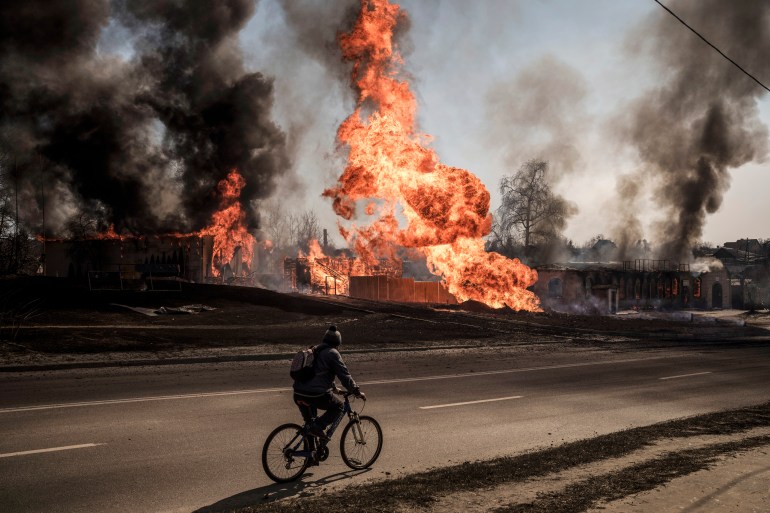 A man rides his bike past flames and smoke rising from a fire following a Russian attack in Kharkiv