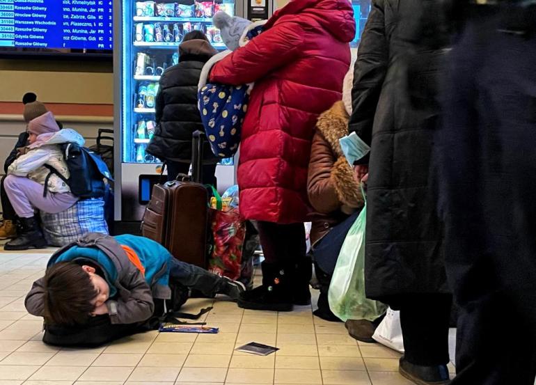A photo of a line of people and a child sleeping on the floor next to them.