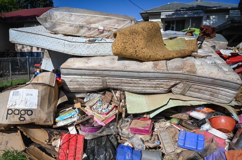 Mattresses, furniture and other possessions ruined by floods piled by the road side in Lismore