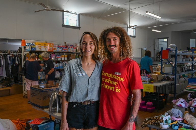 Mark Isaac, in a red t-shirt, and his partner stand in front of the supplies they've gathered to help those affected by the floods