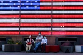 People in masks sit beneath an American flag
