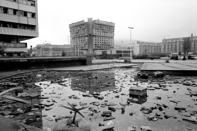 A black and white photograph shows destruction around the Holiday Inn hotel in Sarajevo